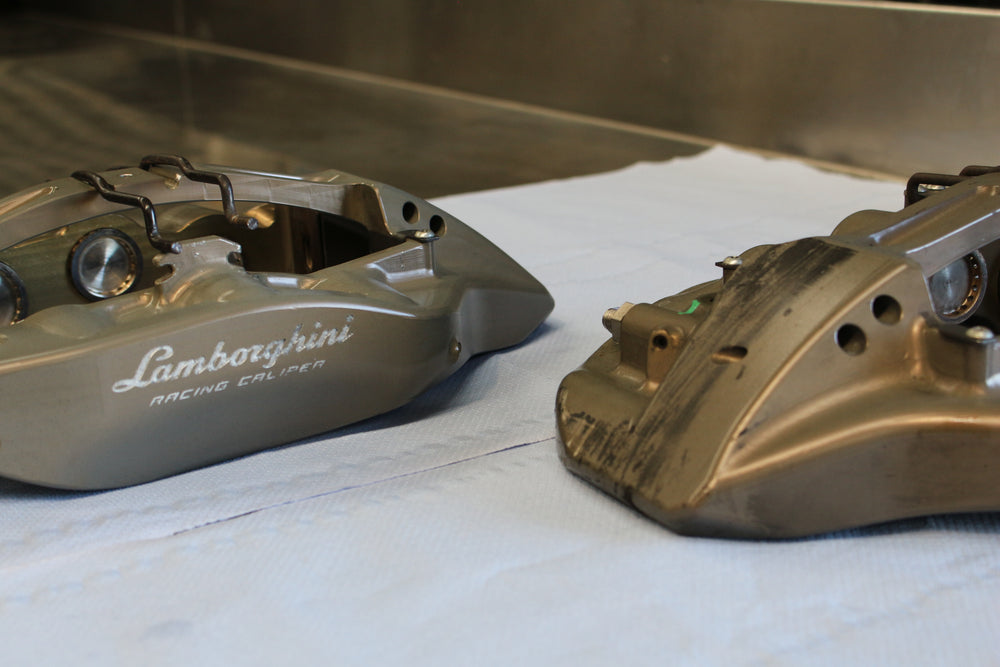 Two metallic car brake calipers on a white surface, with one labeled 'Lamborghini'.