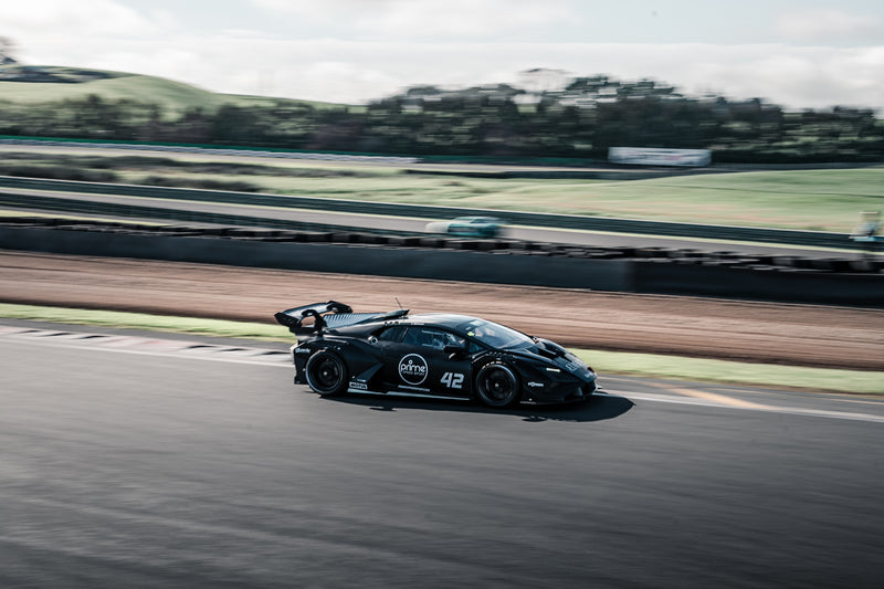 Black sports car, Lamborghini Super Trofeo, racing at Hampton Downs International Motorsport Park, with blurred background
