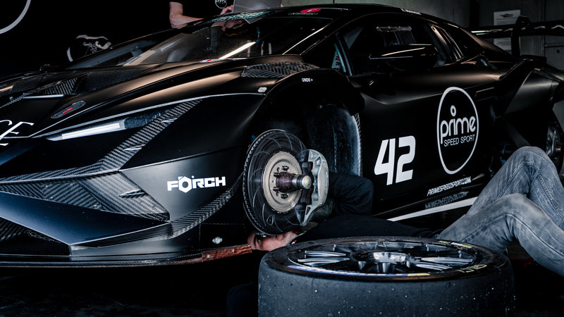 Black Lamborghini Super Trofeo Evo 2, with its wheels off, and mechanics working on the car. 