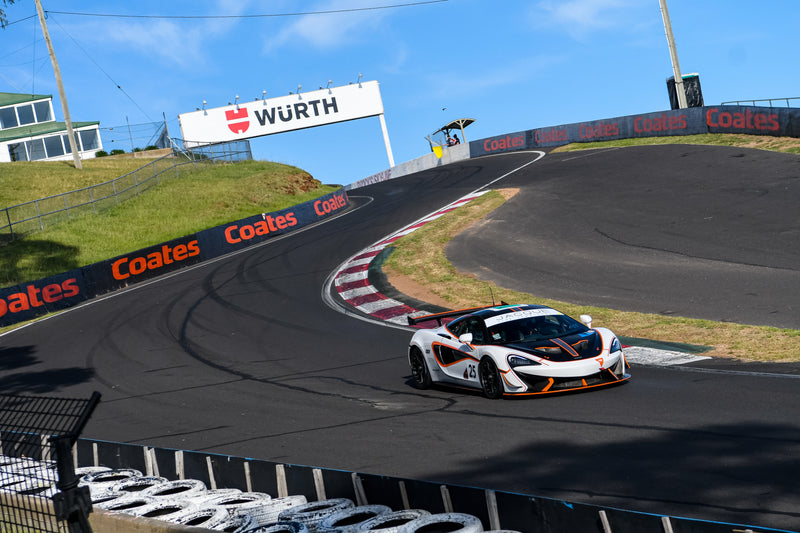 White, black and orange McLaren race car, competing at challenge bathurst at the mount panorama circuit.
