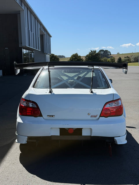 Rear view of a white Subaru Impreza race specked car.