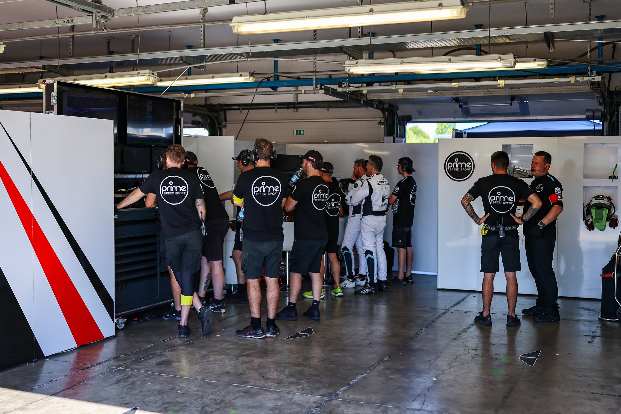 Mechanics in a pit garage with racing drivers.