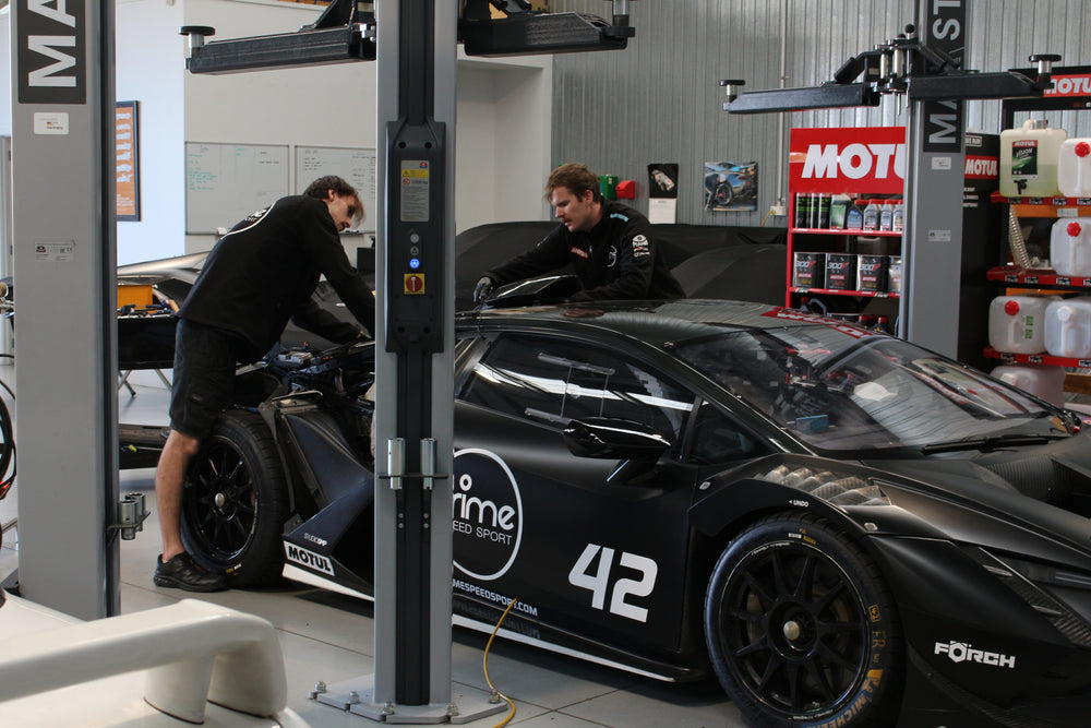 Two mechanics working on a black Lamborghini race car in the Prime Speed Sport Workshop.